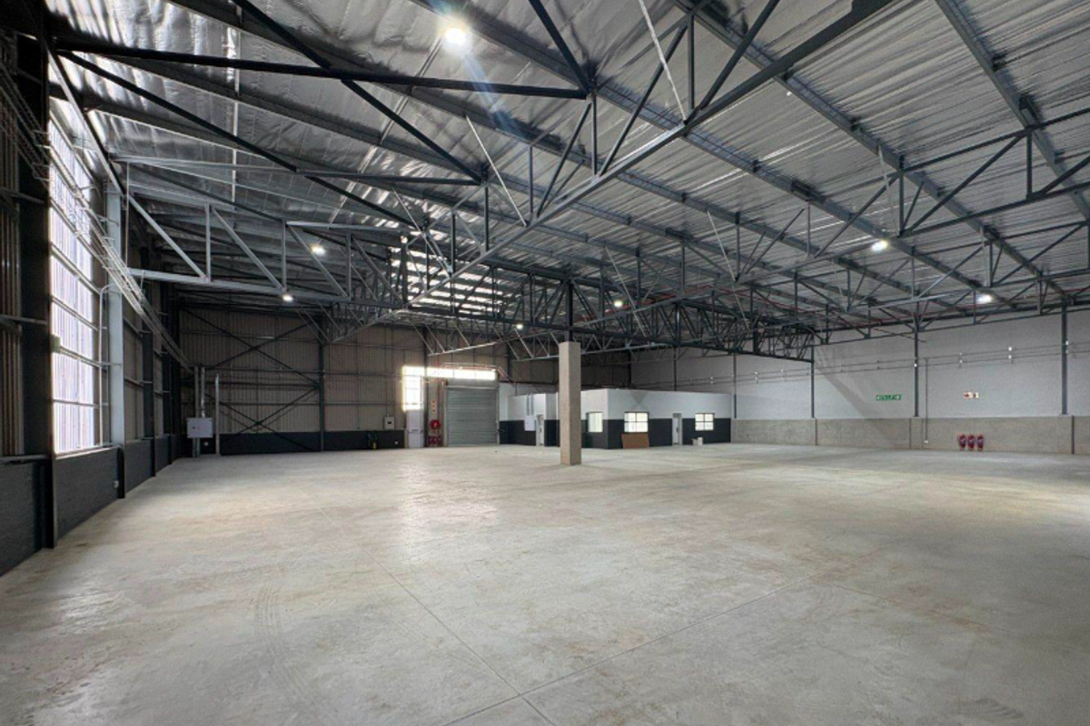 Spacious industrial warehouse featuring high ceilings with exposed steel trusses, polished concrete flooring, and a large roller shutter door for easy access.