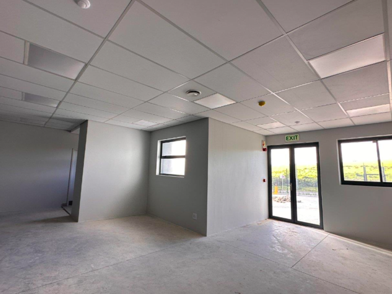 A clean, open-plan industrial office space featuring a suspended ceiling, recessed lighting, concrete flooring, and large aluminium-framed windows and doors.
