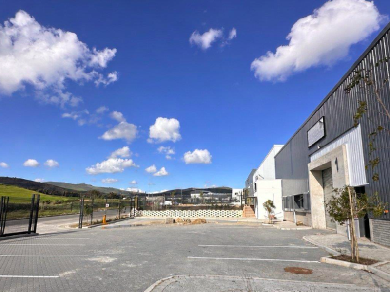Exterior view of an industrial property featuring a modern corrugated metal facade, roller shutter access, and a paved parking area.