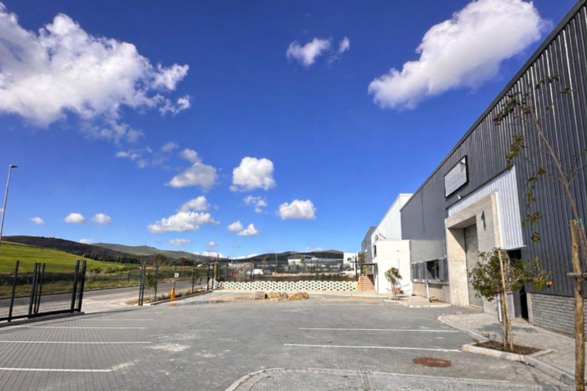 Exterior view of an industrial property featuring a modern corrugated metal facade, roller shutter access, and a paved parking area.