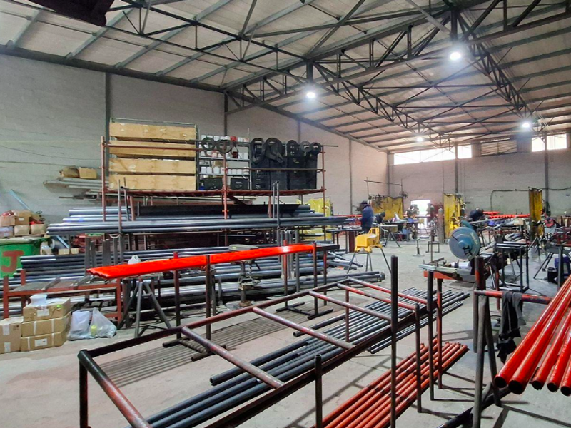 Spacious industrial workshop featuring exposed steel roof trusses, concrete flooring, and high-bay lighting, currently utilized for metal fabrication and storage.