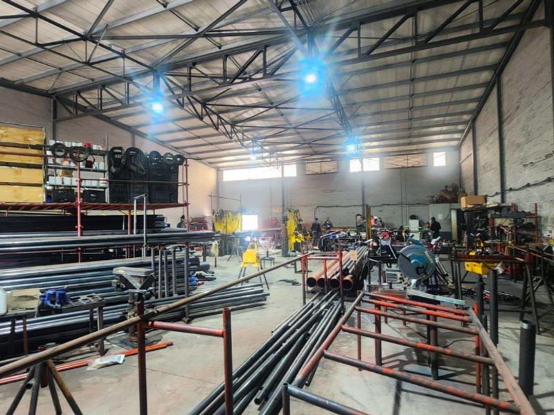 Spacious industrial workshop featuring high-clearance ceilings with exposed steel trusses, concrete flooring, and functional open-plan layout suitable for manufacturing or storage operations.