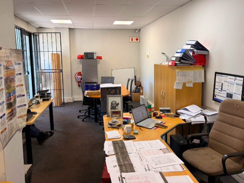 A functional office space featuring a suspended ceiling, security gate, and fire safety equipment, suitable for administrative or industrial business operations.