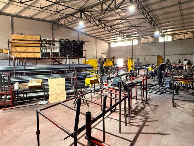 Spacious industrial warehouse featuring exposed steel roof trusses, high-bay lighting, and durable concrete flooring, currently utilized as a functional workshop space.