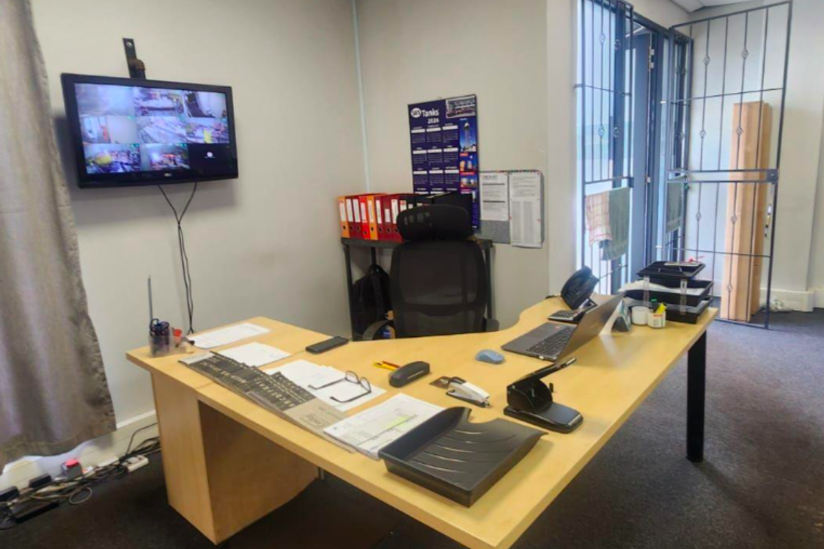 A functional industrial office space featuring a drop ceiling, security gate, and wall-mounted CCTV monitoring system.