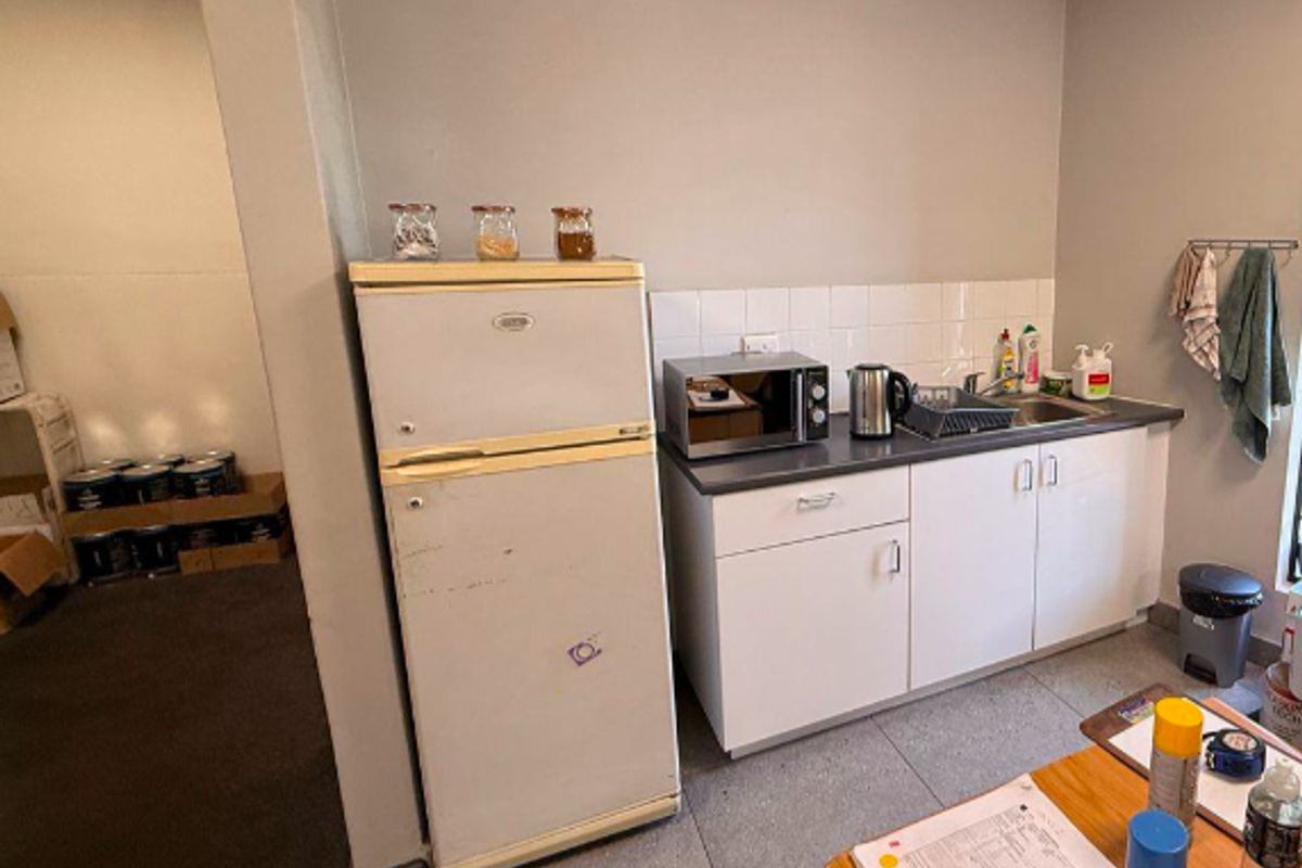 A functional kitchenette area featuring white cabinetry, a tiled backsplash, and a stainless steel sink, suitable for an industrial office or utility space.