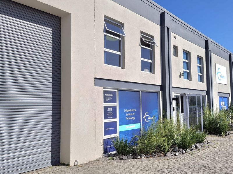Modern industrial unit featuring a large roller shutter door, paved driveway, and professional glass storefront with prominent signage.