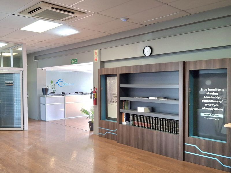 Professional office reception area featuring laminate flooring, a built-in shelving unit, a reception desk, and integrated ceiling-mounted air conditioning.