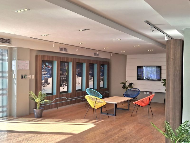 A modern, well-lit industrial office lounge area featuring built-in display cabinetry, recessed lighting, and durable laminate flooring.