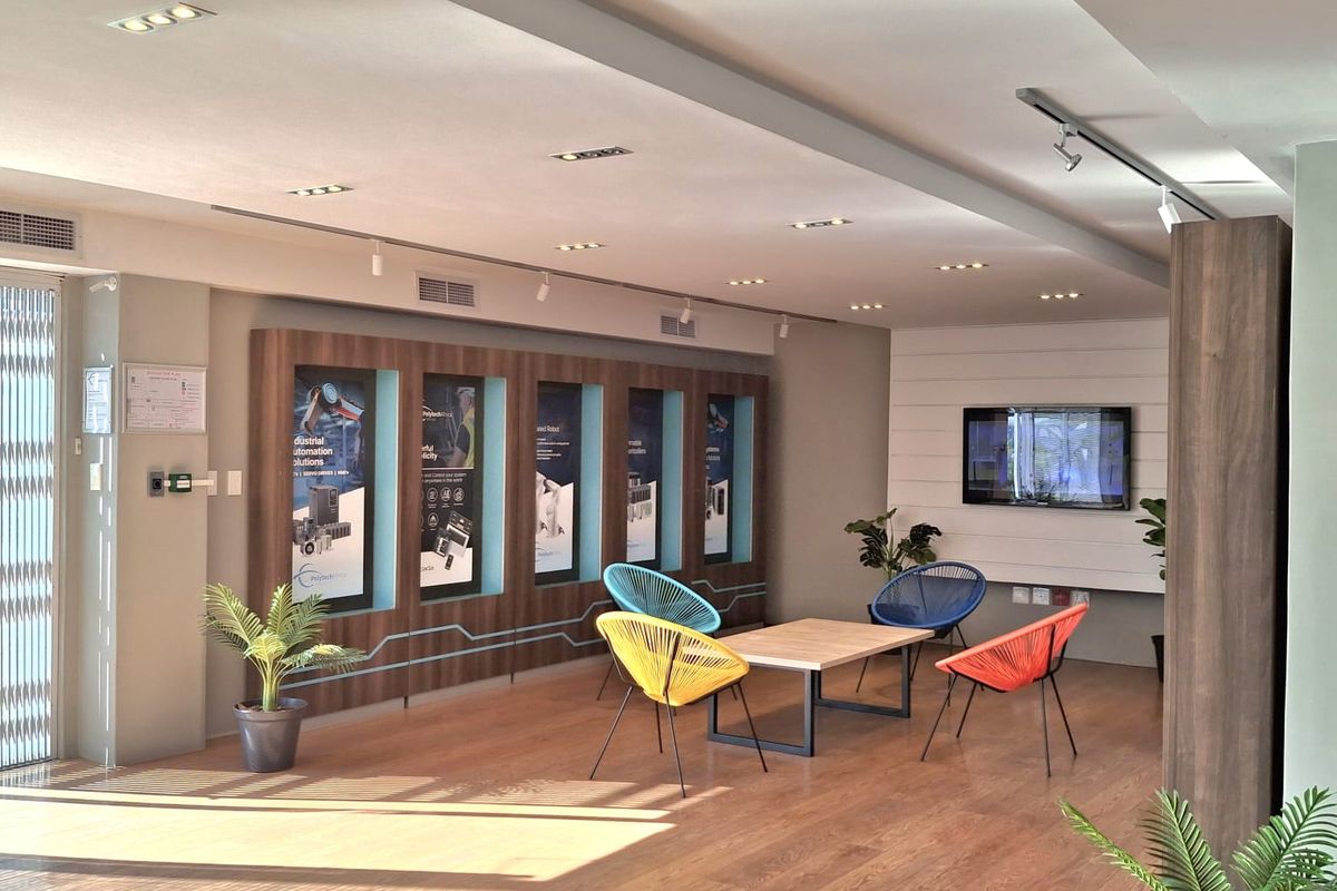 A modern, well-lit industrial office lounge area featuring built-in display cabinetry, recessed lighting, and durable laminate flooring.