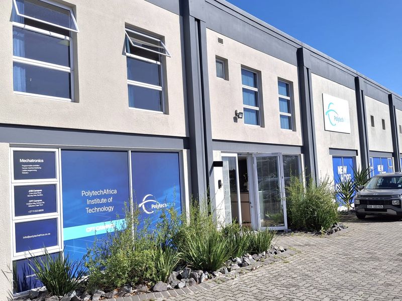 Front elevation of a modern industrial building featuring paved driveway, large glass windows with branding, and well-maintained exterior finishes.