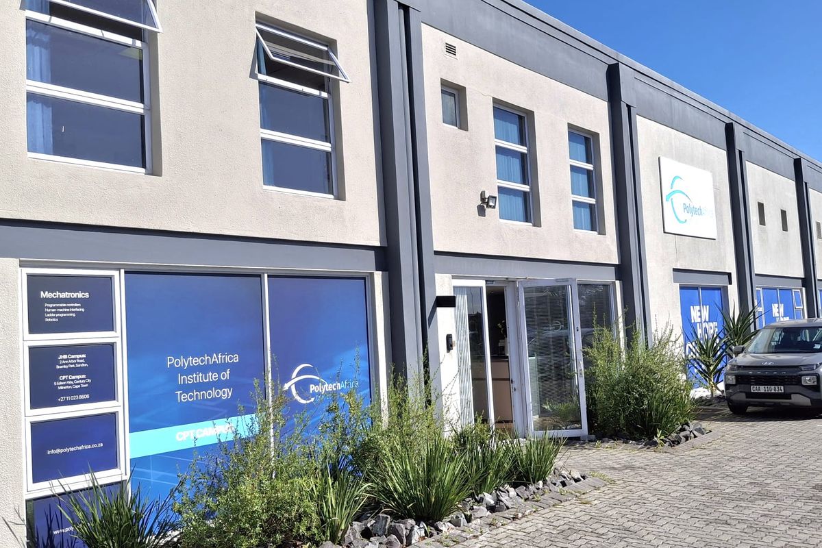 Front elevation of a modern industrial building featuring paved driveway, large glass windows with branding, and well-maintained exterior finishes.