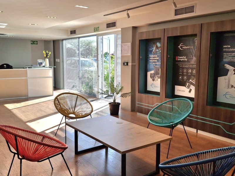 Modern industrial reception area featuring a reception desk, built-in product display cabinets, laminate flooring, and large sliding glass doors providing natural light.
