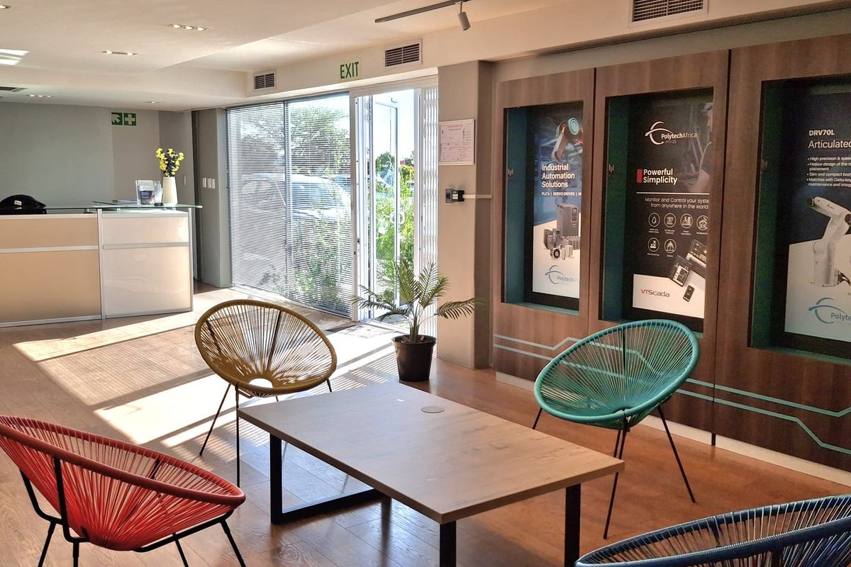Modern industrial reception area featuring a reception desk, built-in product display cabinets, laminate flooring, and large sliding glass doors providing natural light.
