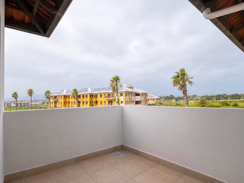 A clean, covered balcony featuring tiled flooring, a drainage point, and a solid balustrade, offering an open view of the surrounding estate.