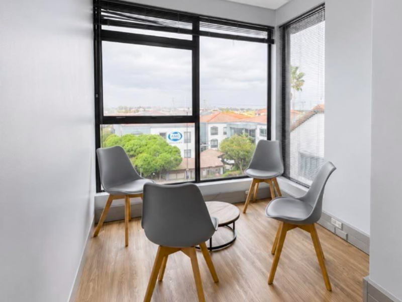 A bright, modern office space featuring large windows with natural light, laminate flooring, and a clean, professional finish.