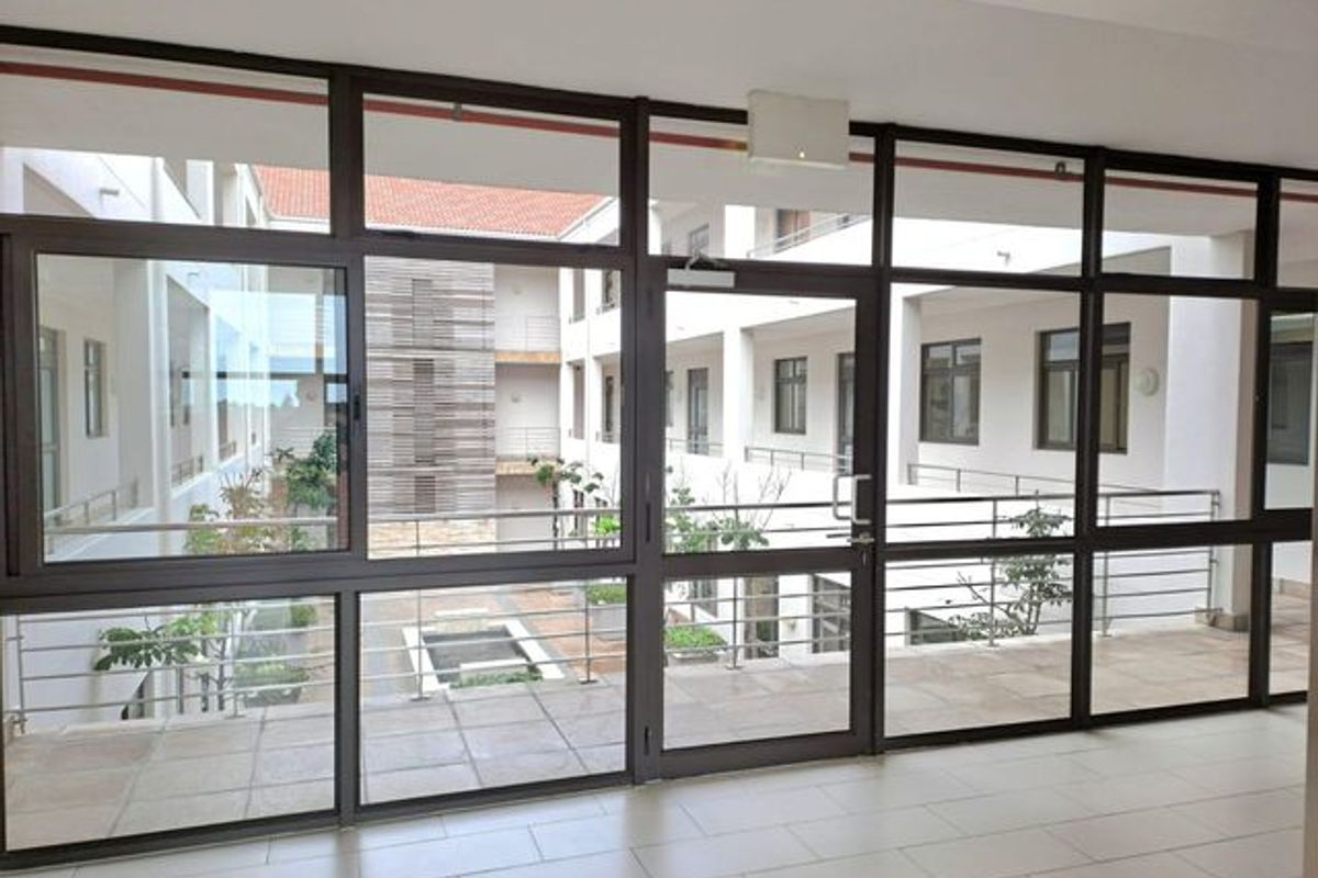 A bright, modern office hallway featuring extensive aluminium-framed glass partitioning and tiled flooring, overlooking an internal courtyard.