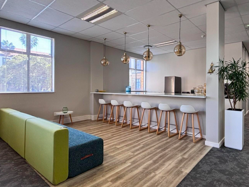 Modern office break-out area featuring a built-in counter, pendant lighting, suspended ceiling, and a mix of laminate and carpet flooring.