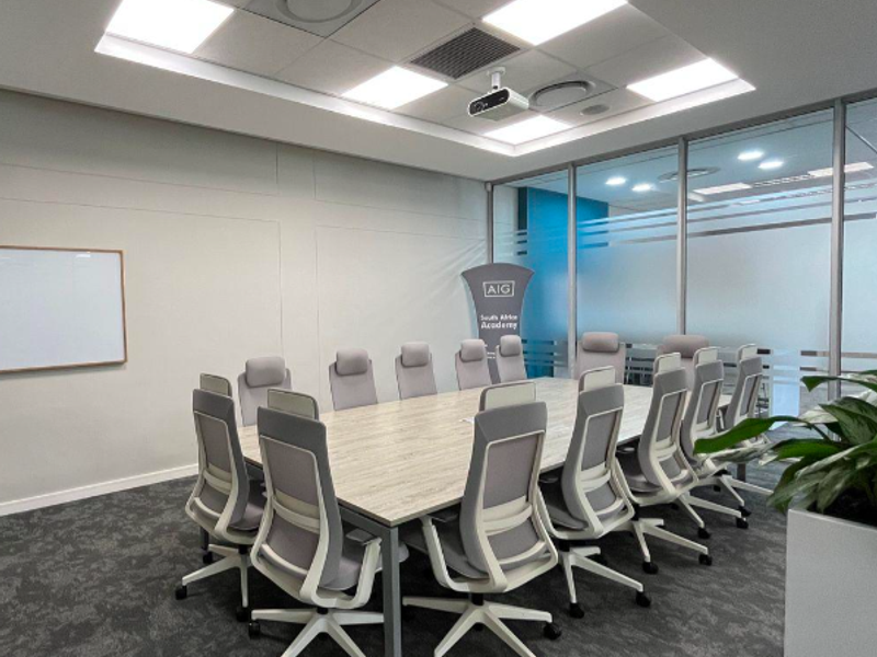 A modern, well-lit professional boardroom featuring a large conference table, glass partition walls, integrated projector, and whiteboard, suitable for corporate meetings.