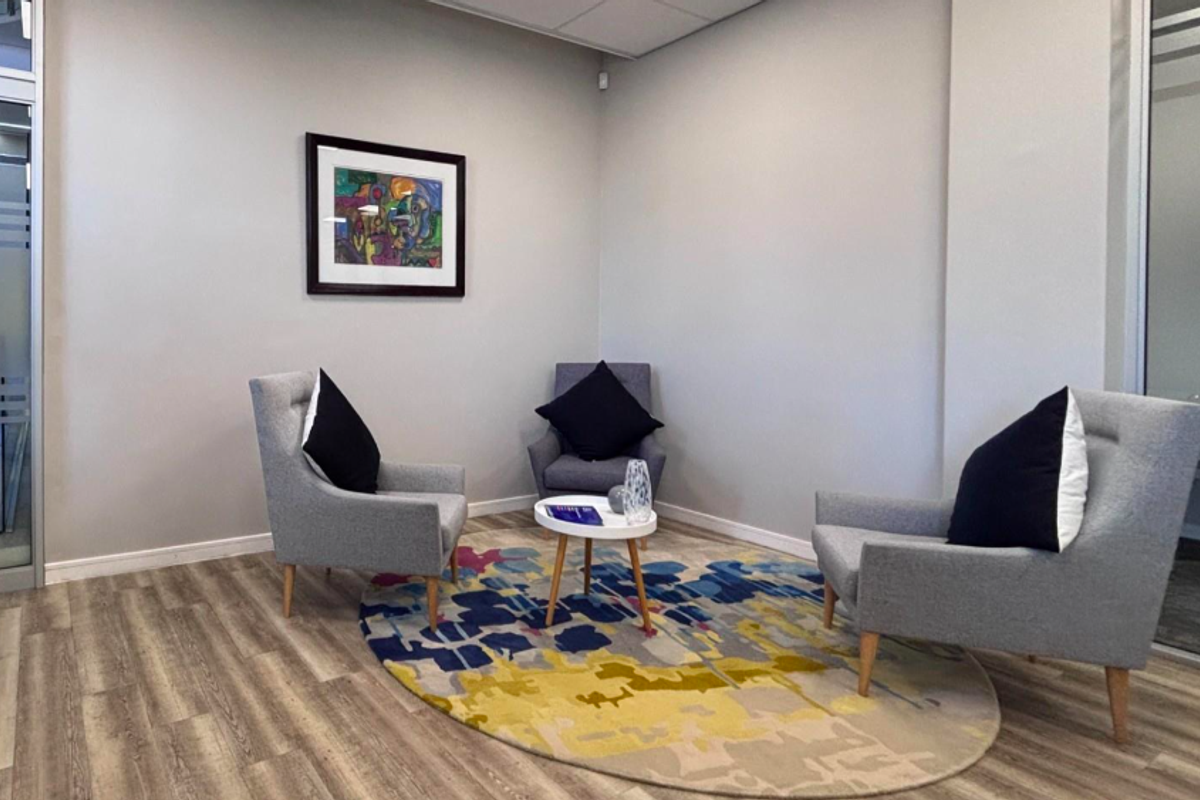 A modern office breakout area featuring wood-look laminate flooring, neutral walls, and a glass partition wall, creating a professional and bright workspace.