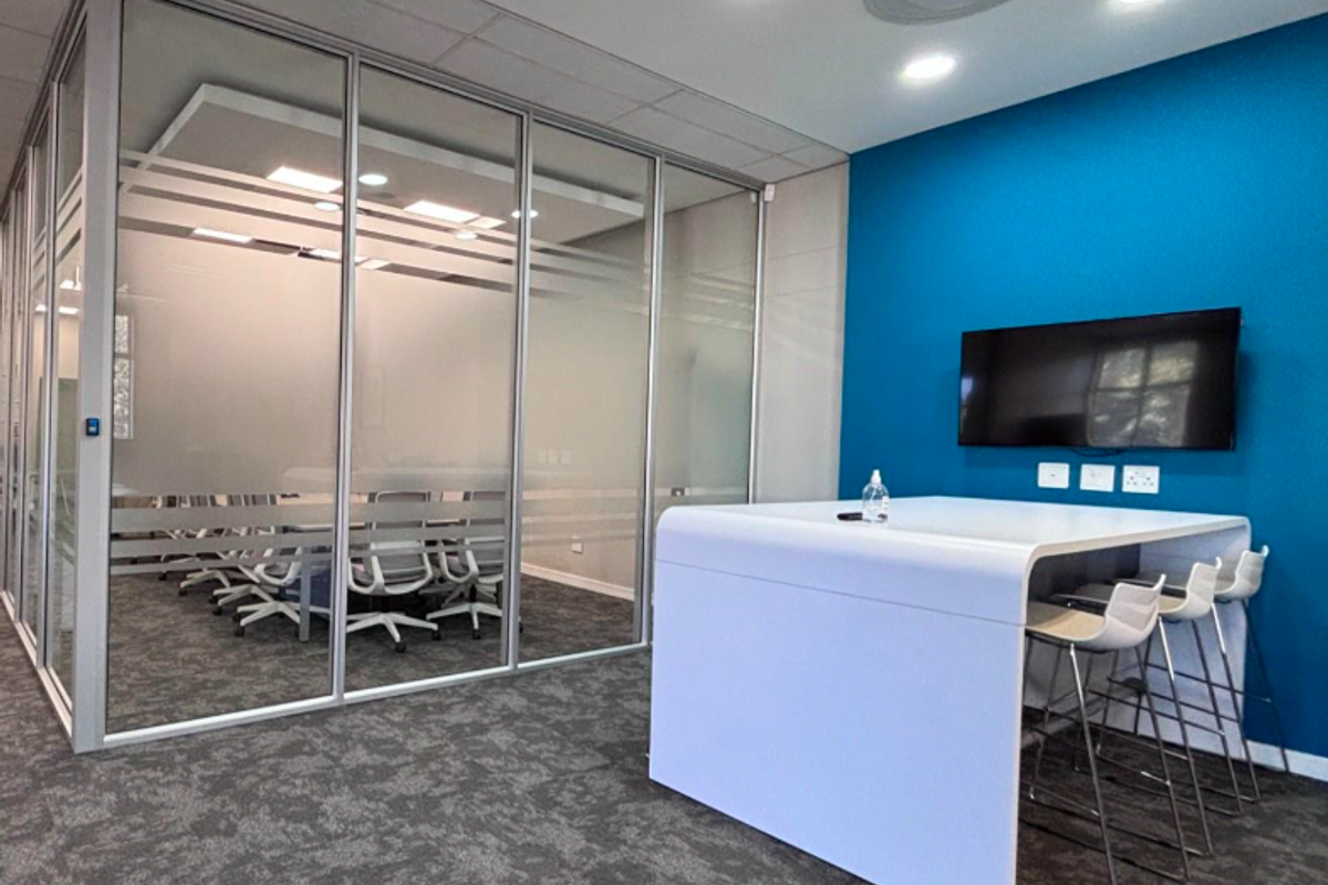 Modern office space featuring a glass-partitioned meeting room, blue accent wall, integrated ceiling lighting, and professional carpeted flooring.