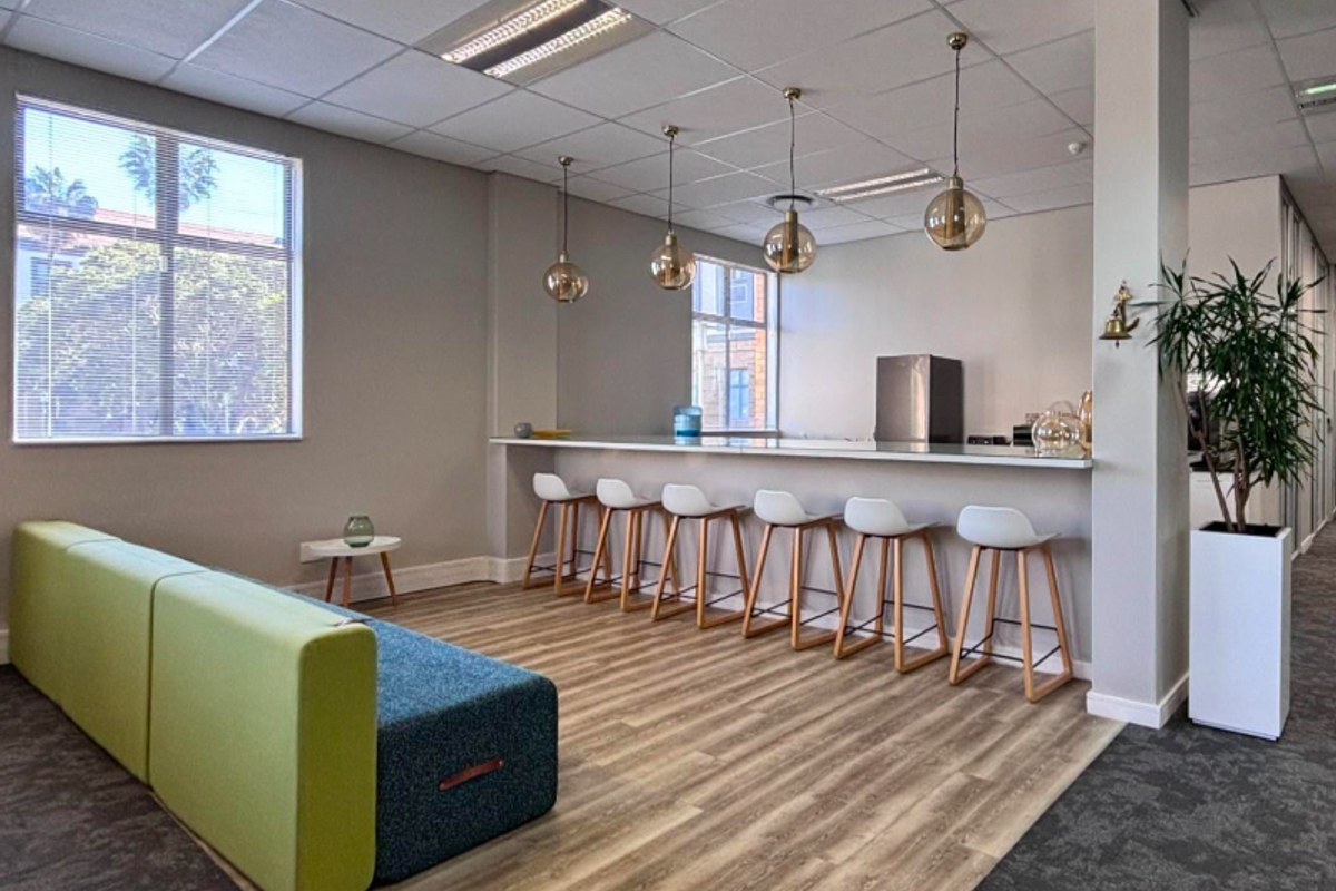 Modern office break-out area featuring a built-in counter, pendant lighting, suspended ceiling, and a mix of laminate and carpet flooring.