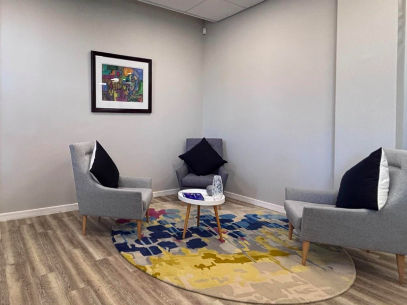 A modern office breakout area featuring wood-look laminate flooring, neutral walls, and a glass partition wall, creating a professional and bright workspace.
