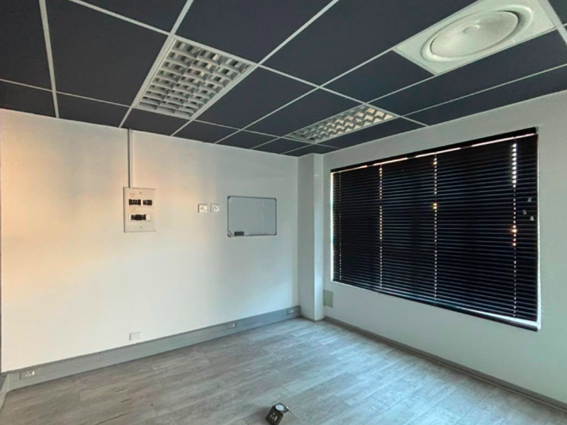 A clean, empty office space featuring a modern suspended ceiling, recessed lighting, air conditioning, and large windows with fitted venetian blinds.