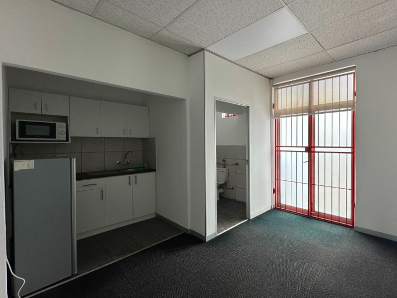 Open plan office space featuring a compact kitchenette, drop ceiling, and secure access door leading to a private restroom area.