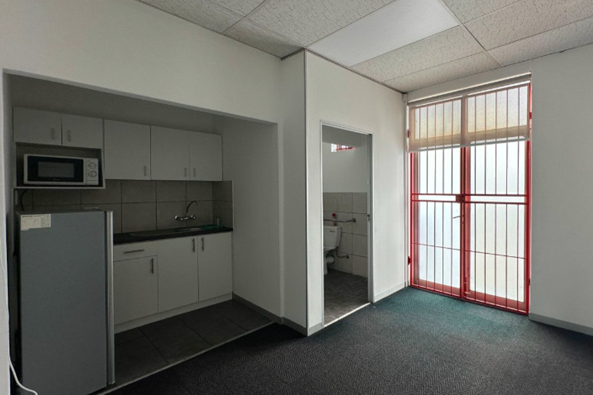 Open plan office space featuring a compact kitchenette, drop ceiling, and secure access door leading to a private restroom area.