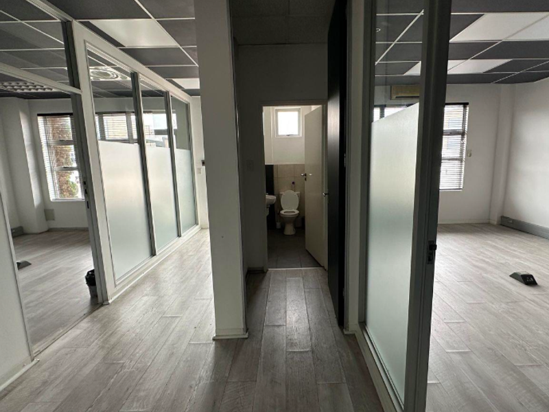 Modern office space featuring glass partitions, suspended ceilings, and wood-look laminate flooring, including a private internal restroom facility.