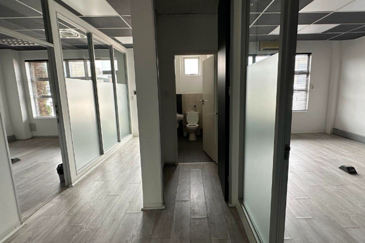Modern office space featuring glass partitions, suspended ceilings, and wood-look laminate flooring, including a private internal restroom facility.