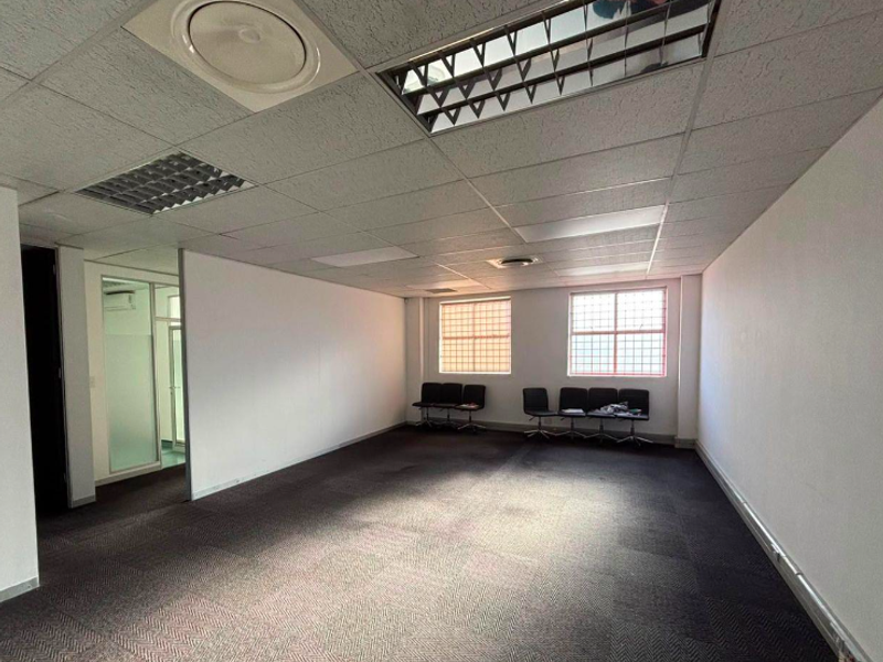 An open-plan office space featuring suspended ceilings with recessed lighting, carpeted flooring, and windows fitted with security bars.