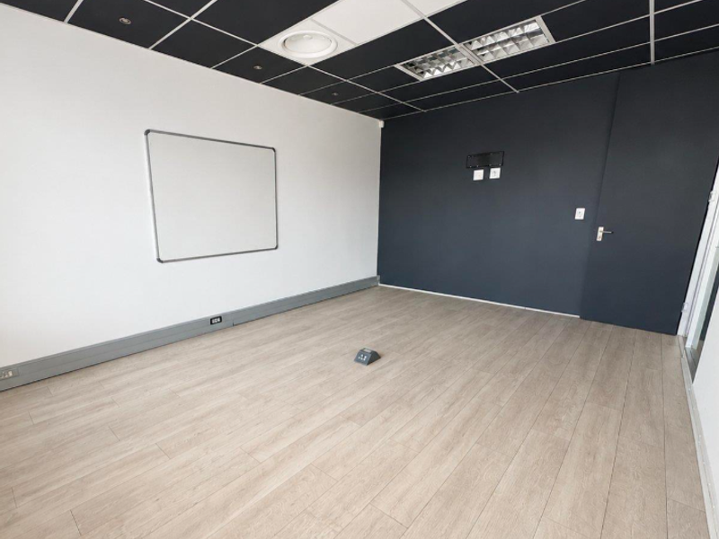 A modern, empty office space featuring light wood-look laminate flooring, a contrasting black suspended ceiling with recessed lighting, and integrated wall-mounted whiteboard.
