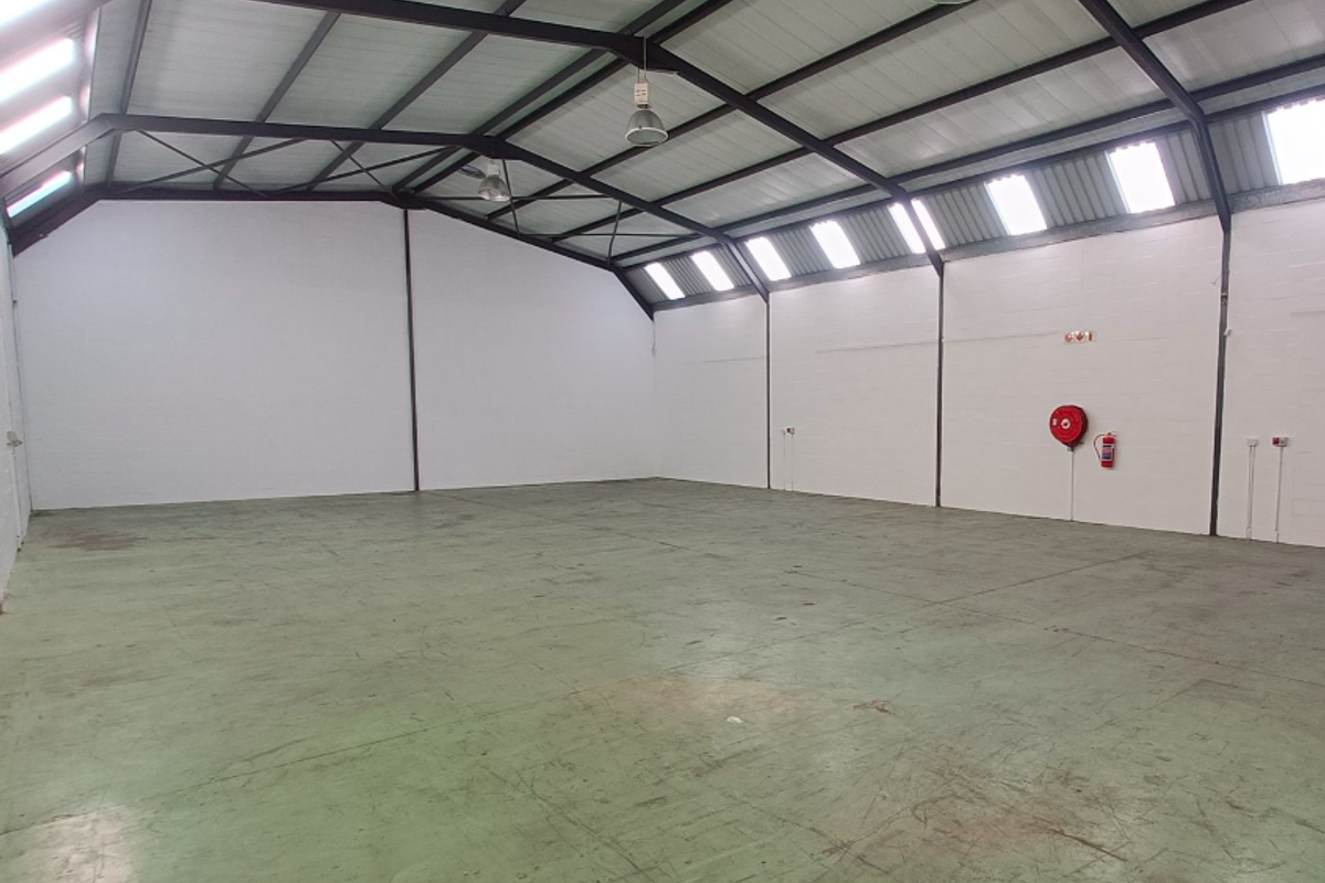 Spacious open-plan office or warehouse area featuring high exposed steel trusses, abundant natural light from skylights, and durable epoxy-coated concrete flooring.