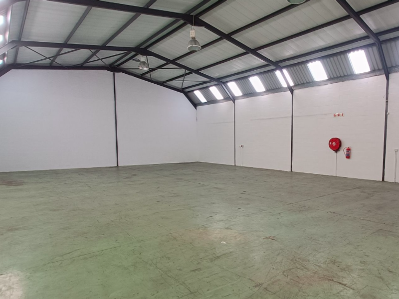 Spacious open-plan office or warehouse area featuring high exposed steel trusses, abundant natural light from skylights, and durable epoxy-coated concrete flooring.