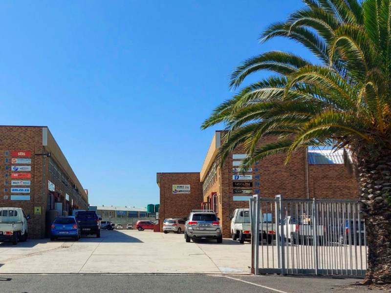 Exterior view of a commercial office park featuring brick buildings, a paved driveway, and secure gated access.