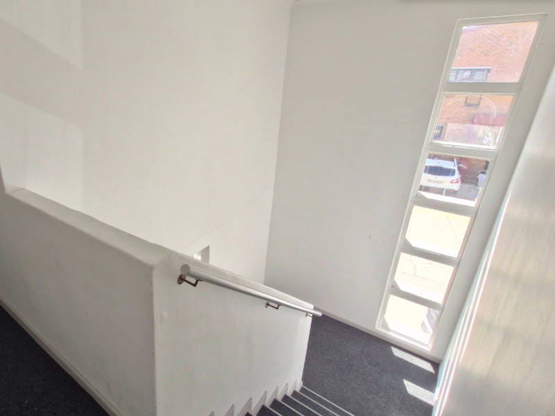 A bright, minimalist stairwell featuring a clean white balustrade, a modern metal handrail, and a tall vertical window providing natural light.