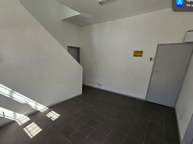 An empty office space featuring tiled flooring, a staircase, and neutral walls, suitable for a professional workspace setup.