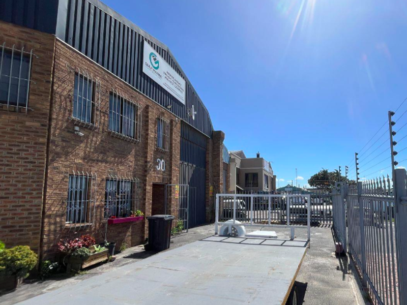 Front exterior view of an industrial warehouse building featuring face brick construction, metal cladding, and secure perimeter fencing with electric security wires.