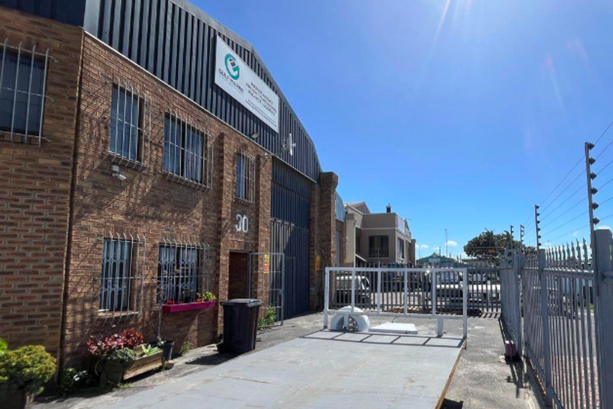 Front exterior view of an industrial warehouse building featuring face brick construction, metal cladding, and secure perimeter fencing with electric security wires.