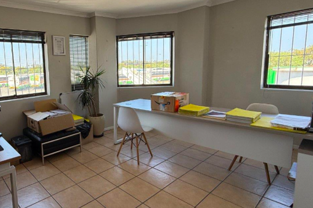 Functional office space featuring ceramic tiled flooring, large windows with security bars, and overhead fluorescent lighting.