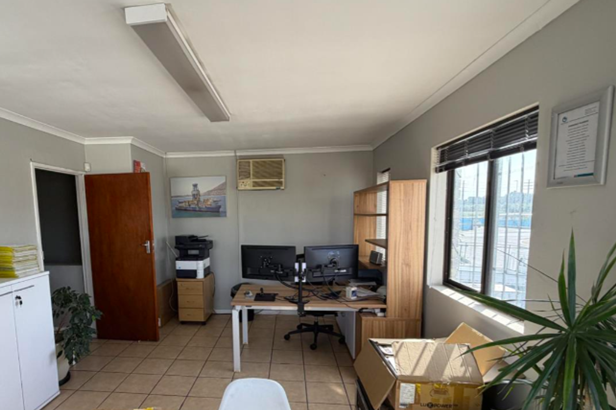 Functional office space featuring tiled flooring, window security bars, and an integrated air conditioning unit, suitable for professional industrial or administrative use.