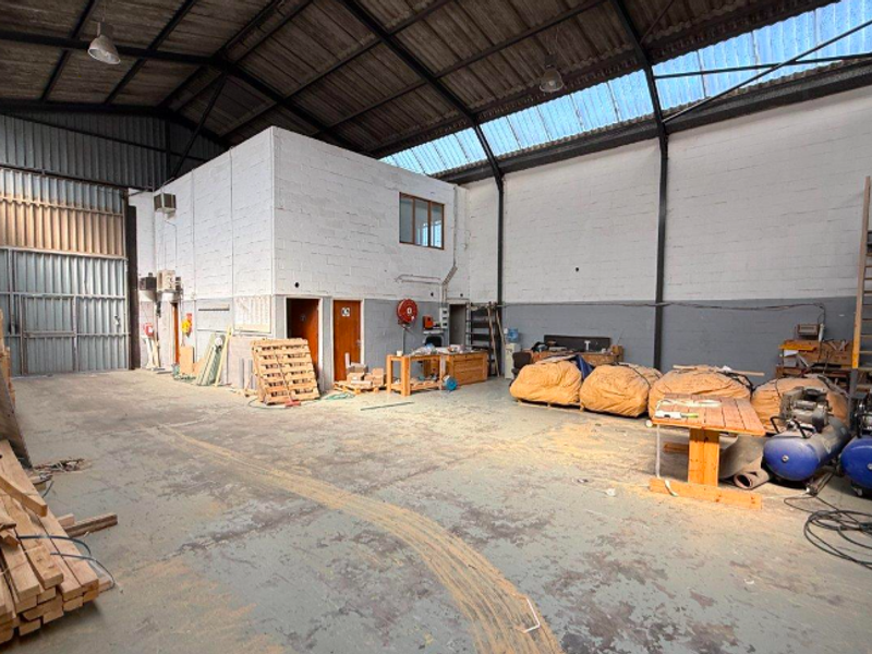 Spacious industrial warehouse unit featuring high ceilings with exposed steel trusses, skylights, concrete flooring, and a mezzanine level, suitable for various commercial or storage uses.