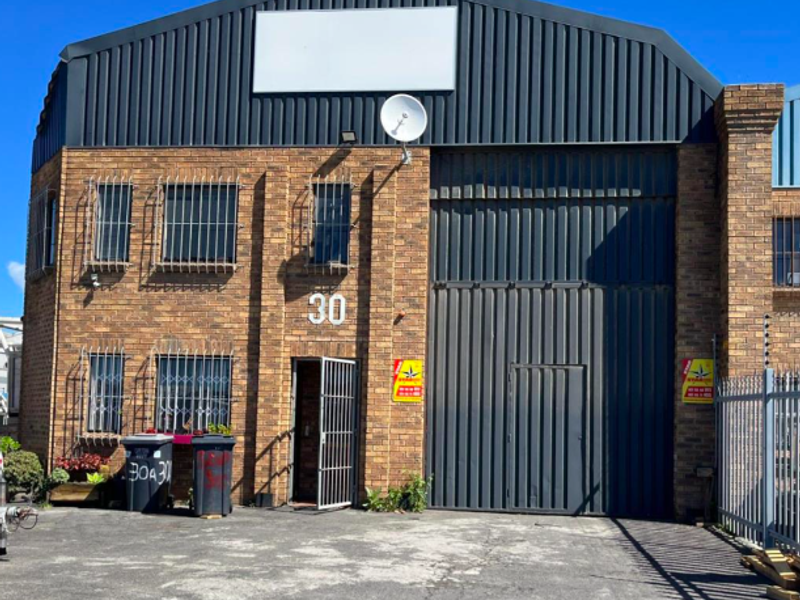 Industrial warehouse unit featuring a face brick facade, large roller door, security bars, and perimeter electric fencing.