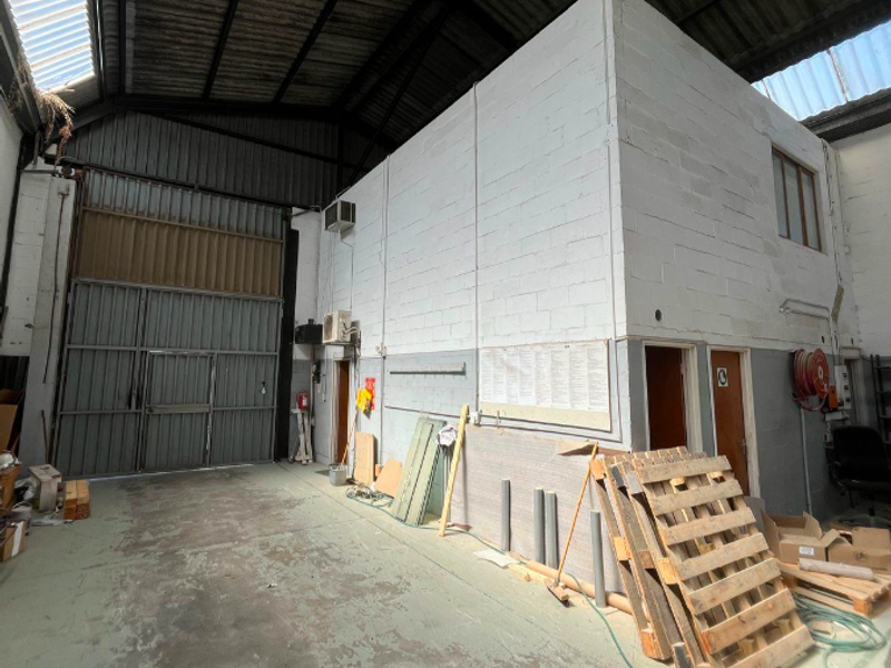 Spacious industrial utility area featuring high ceilings with exposed steel trusses, large roller shutter door, and concrete block wall construction.