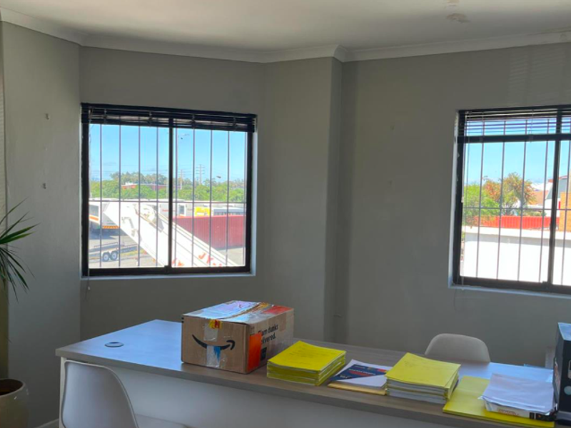 A functional office space featuring built-in desk cabinetry, security bars on windows, and venetian blinds, suitable for a professional industrial workspace.