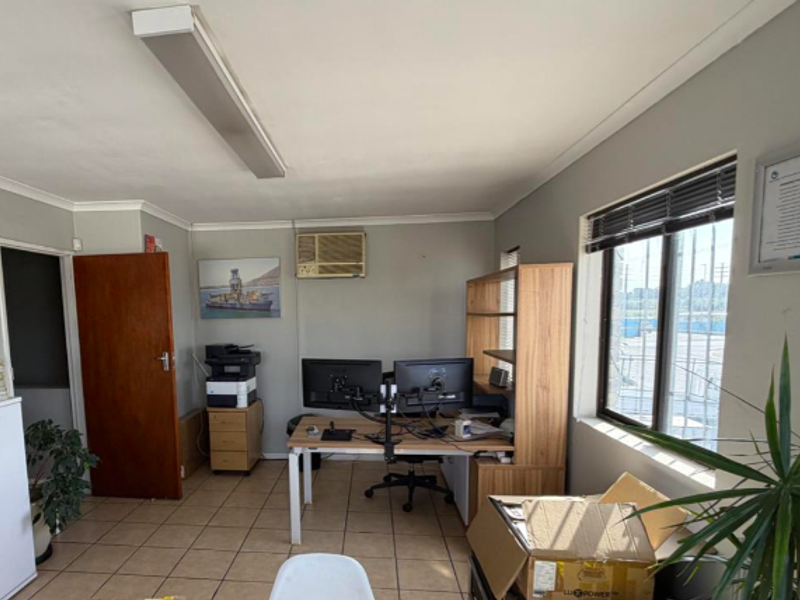 Functional office space featuring tiled flooring, window security bars, and an integrated air conditioning unit, suitable for professional industrial or administrative use.