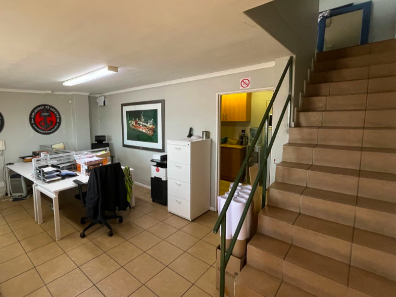 Functional industrial office space featuring tiled flooring, a staircase with a metal handrail, and direct access to an adjacent utility or kitchen area.