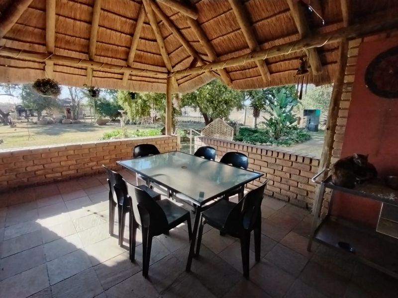 A covered outdoor patio featuring a traditional thatched roof, exposed timber beams, and brick walling, overlooking the farm garden.